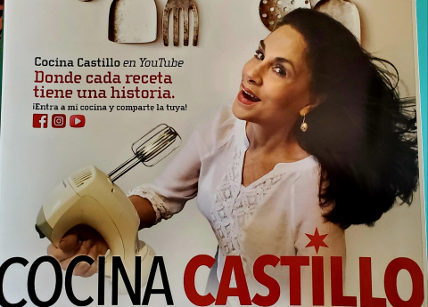 Retiree Nydia Castillo in a promotion for her YouTube Channel, Cocina Castillo. She is holding a hand mixer and wearing a white shirt.